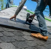 Worker installing shingles on a roof under a bright blue sky