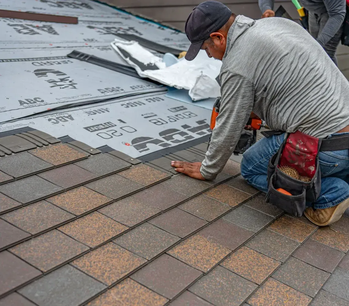 Roofers installing gray underlayment and brown shingles on a rooftop under construction