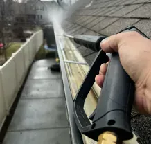 Person spraying water onto a sloped roof with a pressure washer from a balcony or walkway