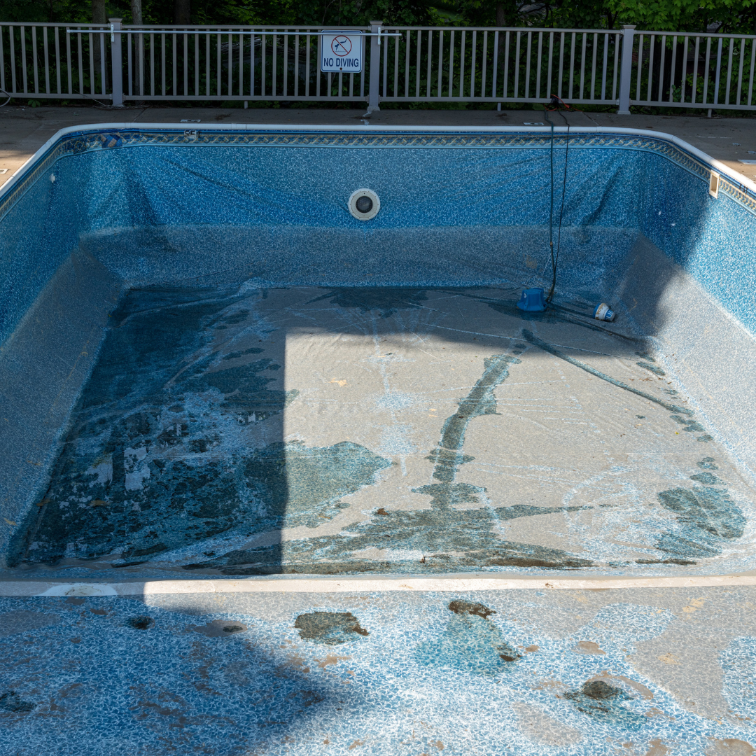 Empty drained swimming pool with blue mosaic walls and a metal fence in the background