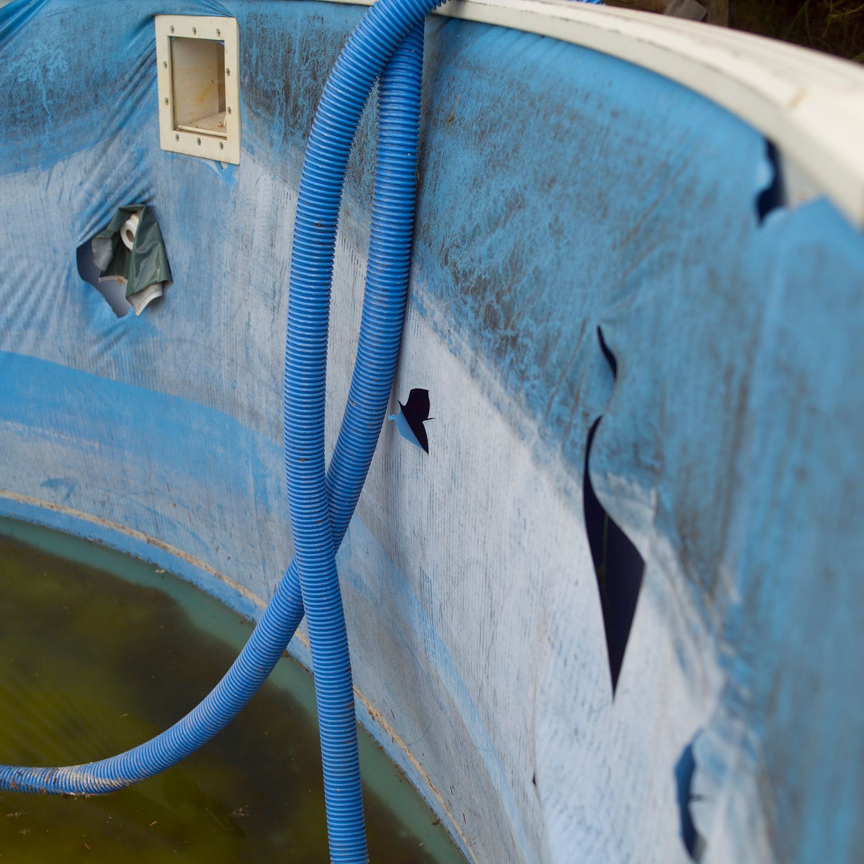 Blue hose draped over the edge of a weathered white pool or tank with peeling paint