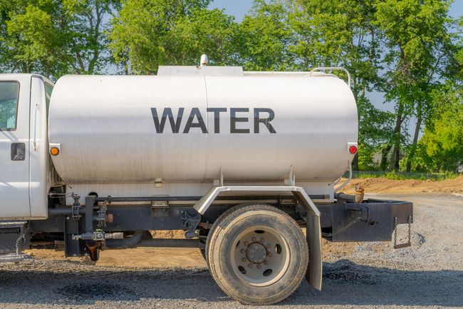 White water tanker truck parked on gravel road with trees in the background
