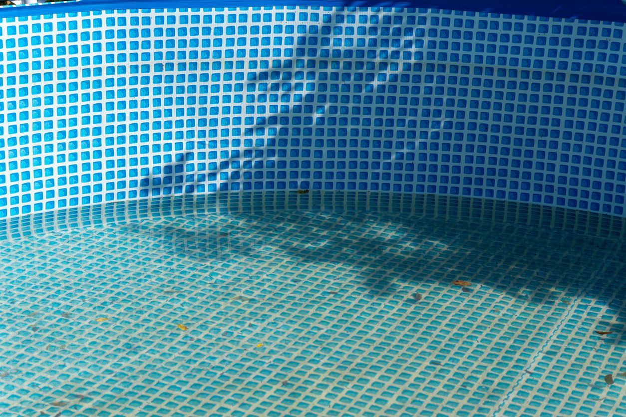 Empty blue-tiled swimming pool with a small water puddle and shadow on the floor