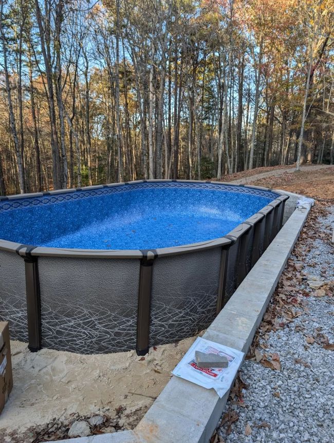 Above-ground pool with blue water in a wooded backyard in autumn