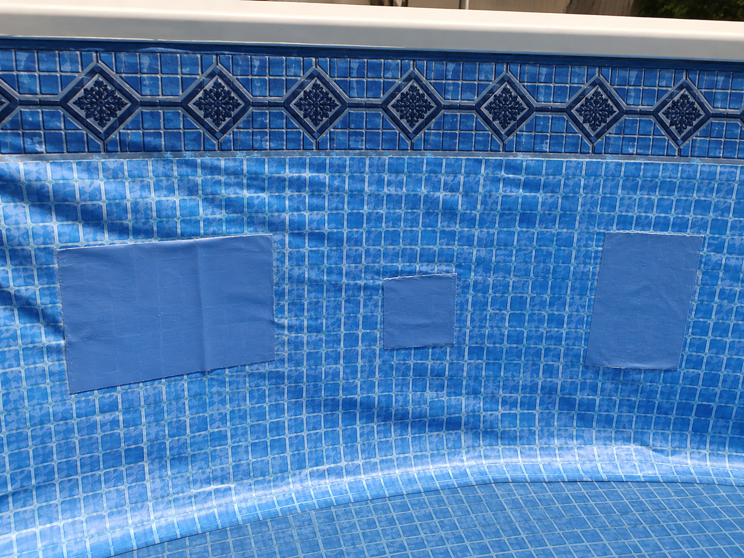 Blue-tiled swimming pool wall with three square patches under the waterline