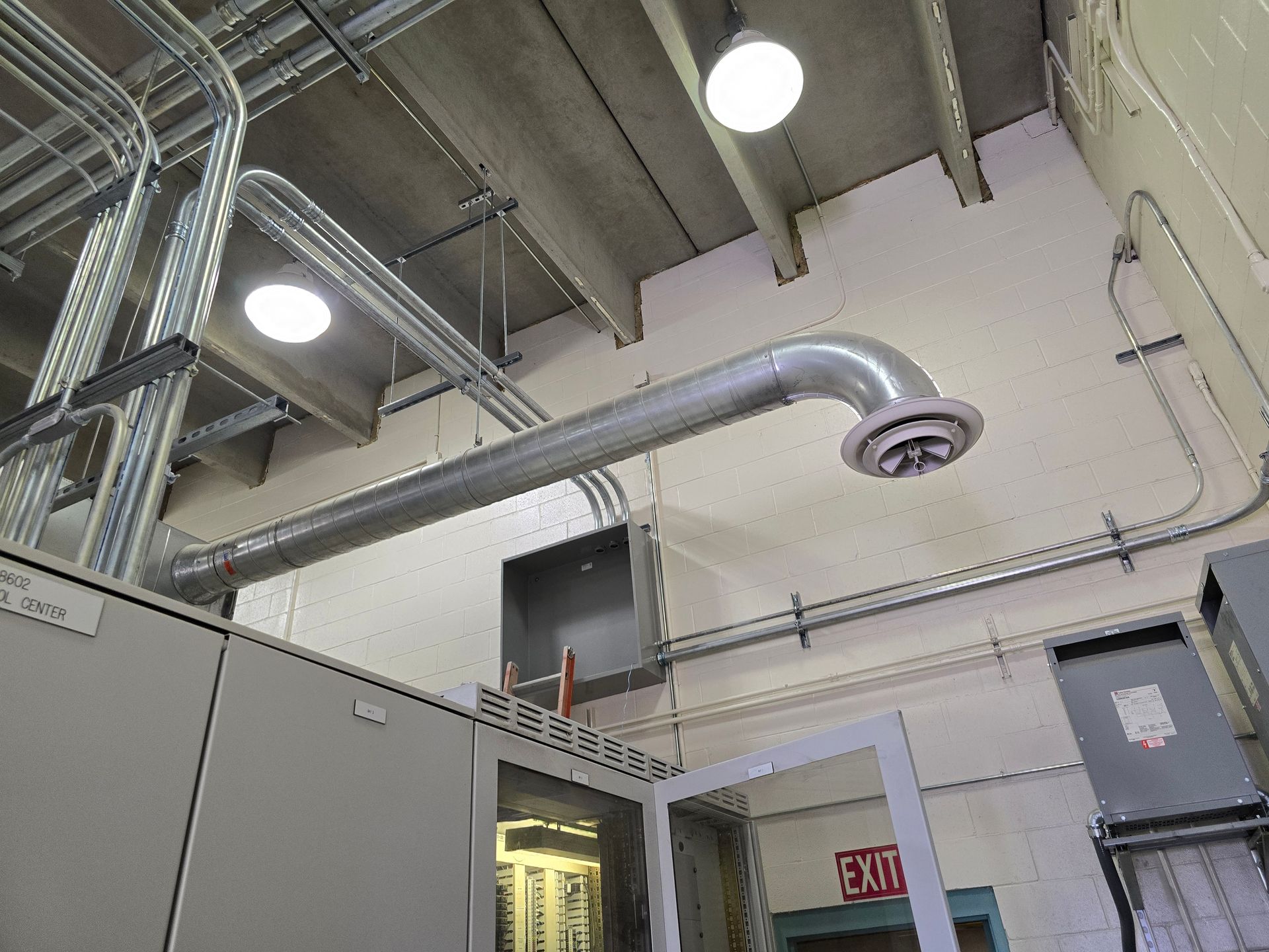 Ceiling with pipes, vents, and lights in an industrial setting. Gray and white with a partially visible door.