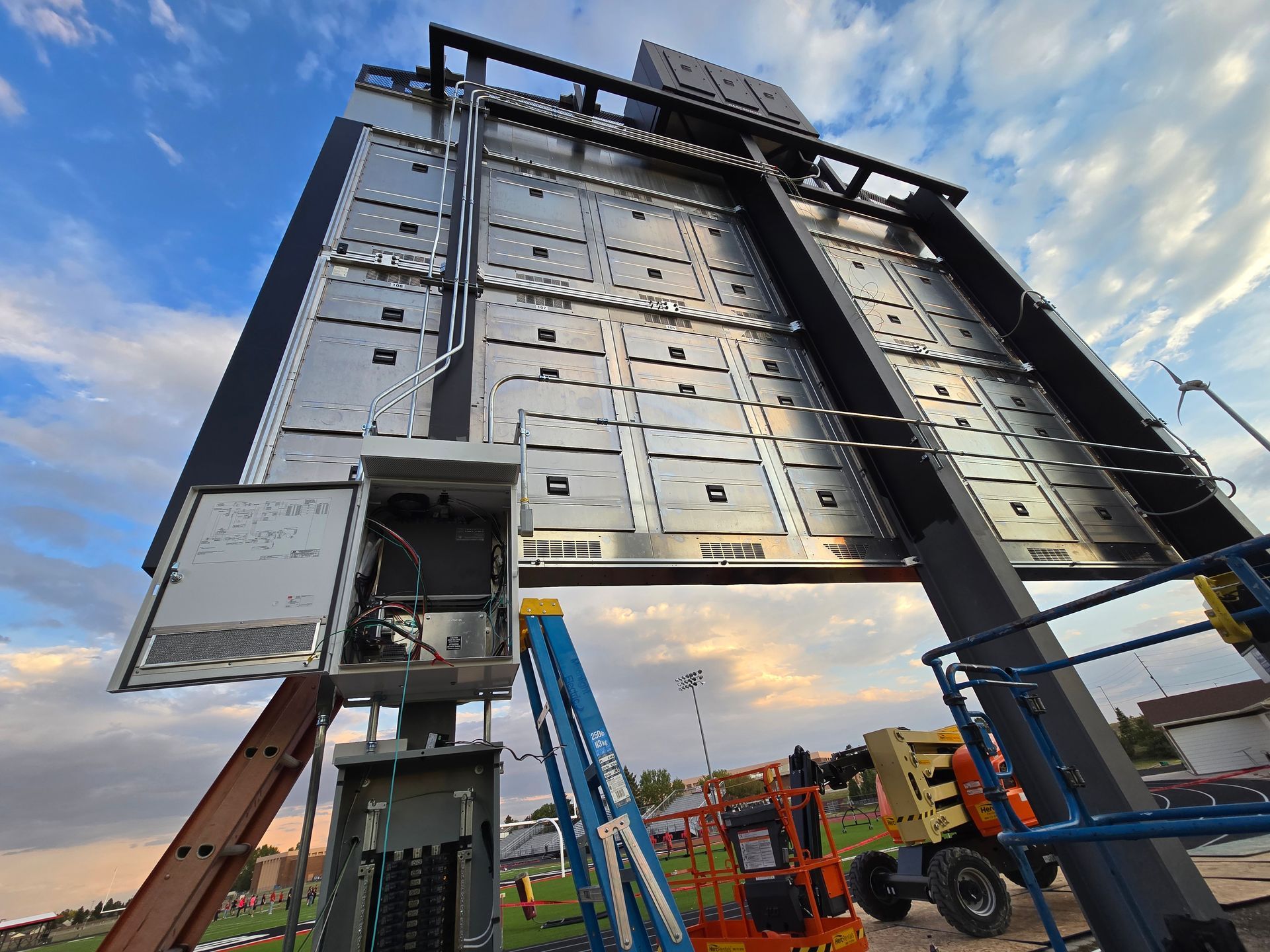 Billboard being worked on by crew, electrical panel open, blue sky.