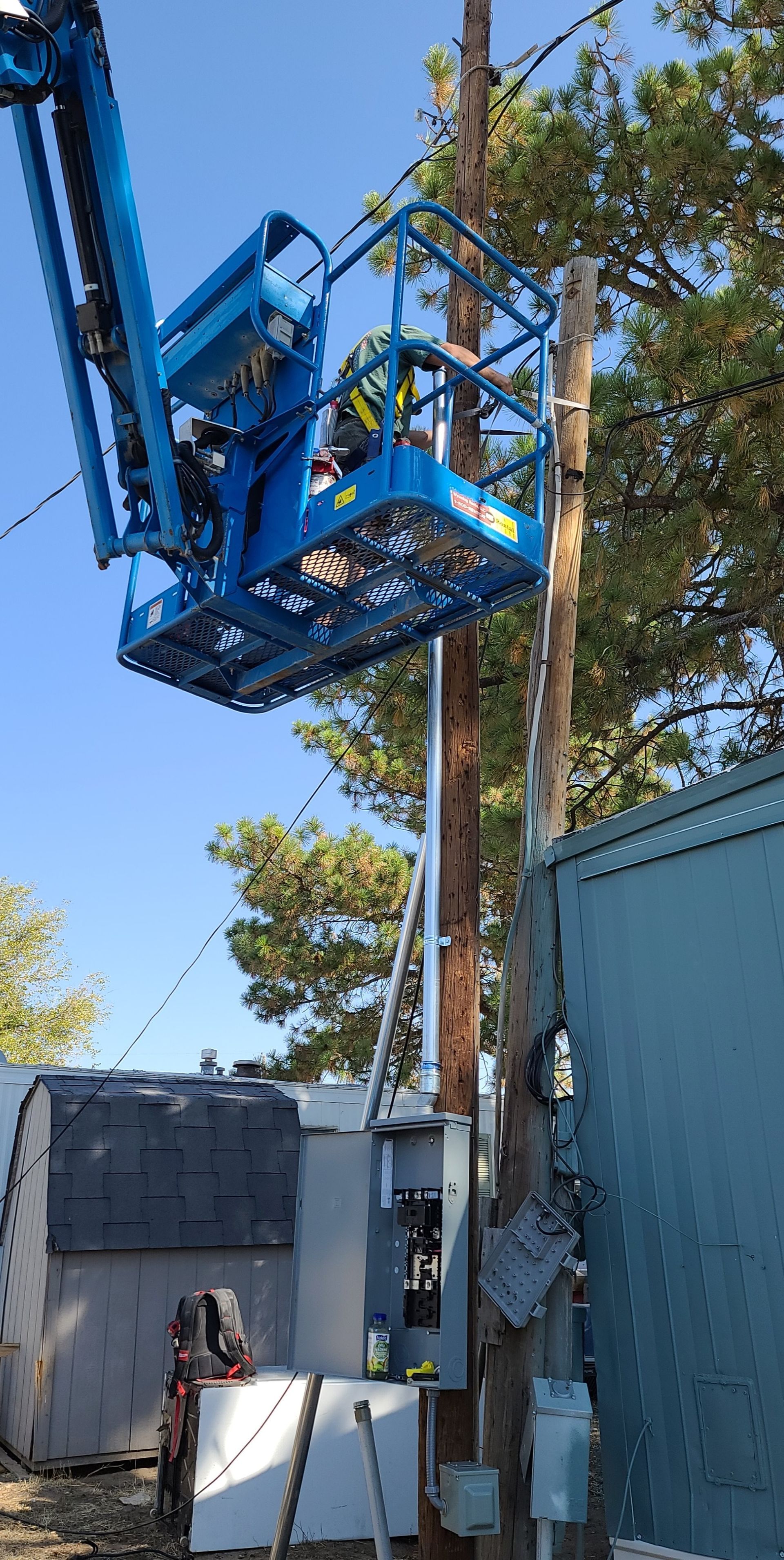 A utility worker in a blue lift truck works on a power pole, surrounded by equipment, with blue sky.