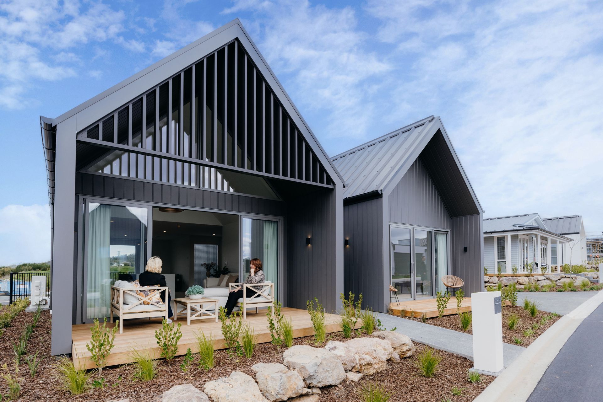 Modern gray houses with outdoor seating on wooden decks under a blue sky.