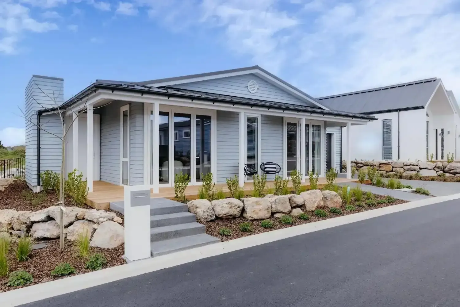 Light blue cottage home with white trim and a small stone retaining wall.