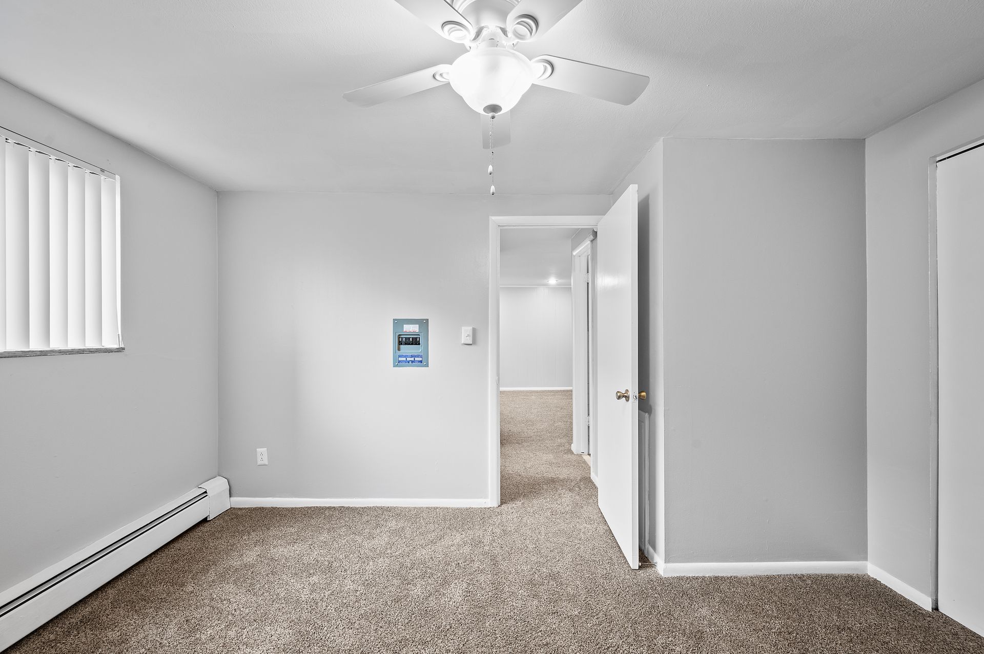 Empty bedroom with gray walls, carpet, and a ceiling fan. Doorways and a window are visible.
