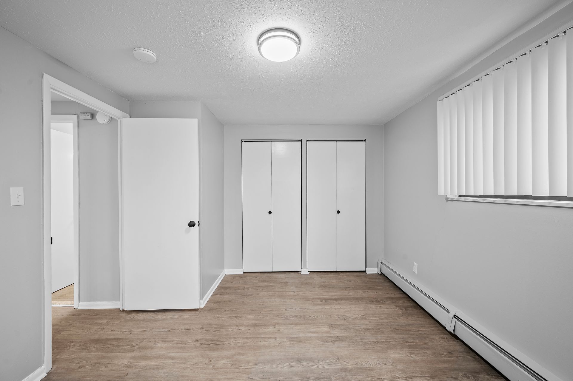 Empty bedroom with gray walls, two white closets, and a window with blinds.