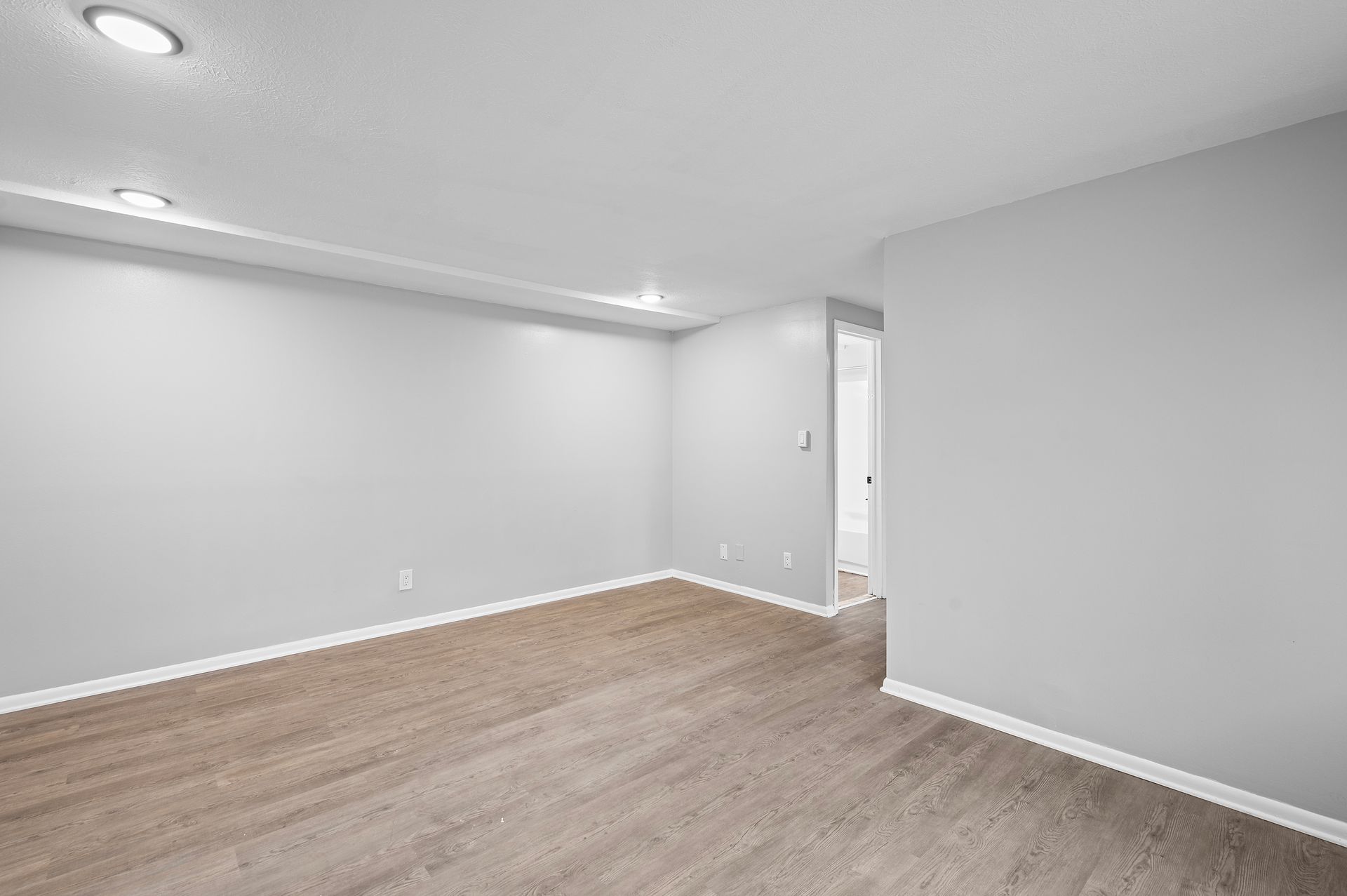 Empty room with light gray walls, recessed lighting, and brown hardwood flooring.