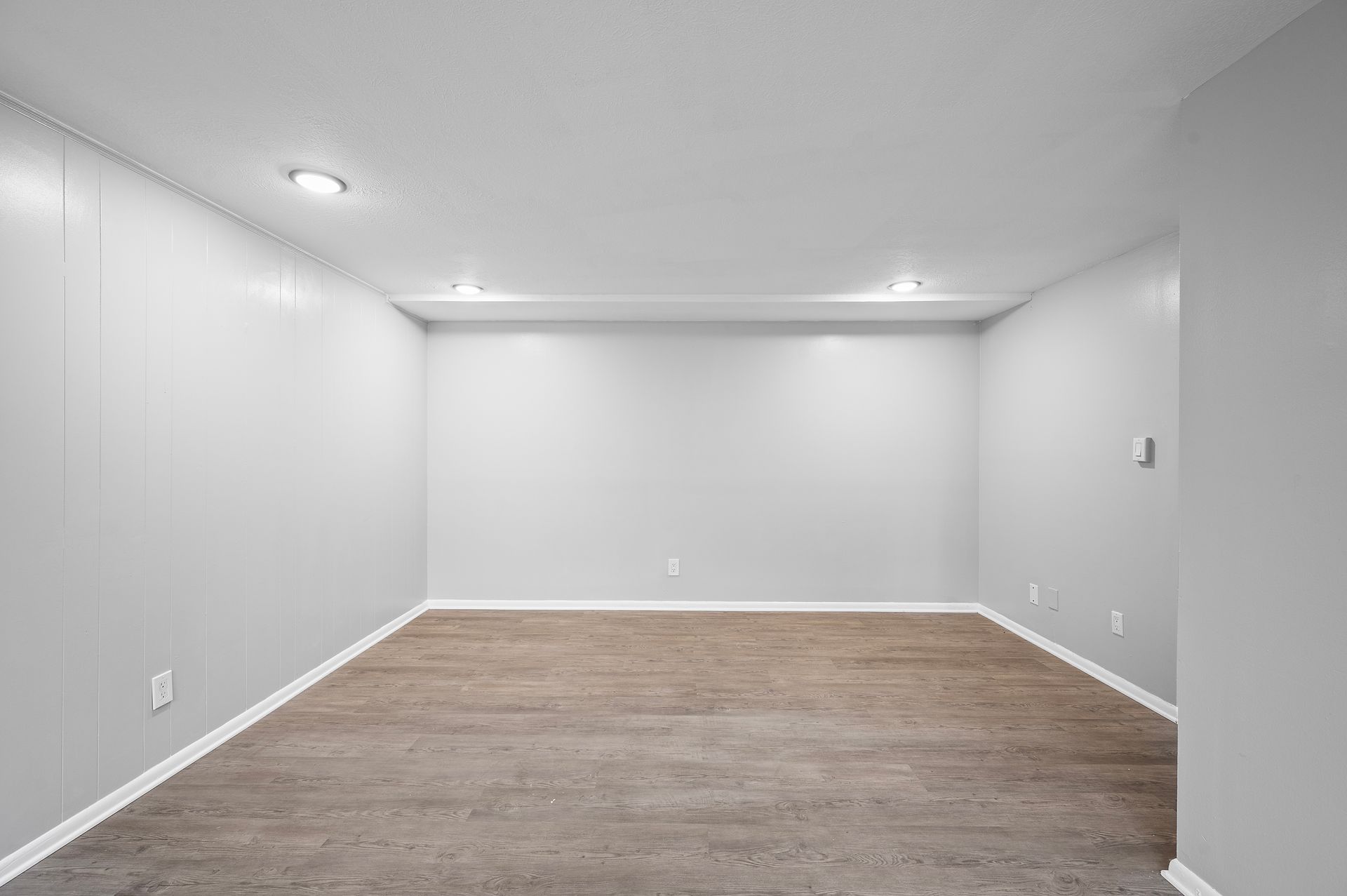 Empty room with light gray walls, recessed lighting, and wood-look flooring.