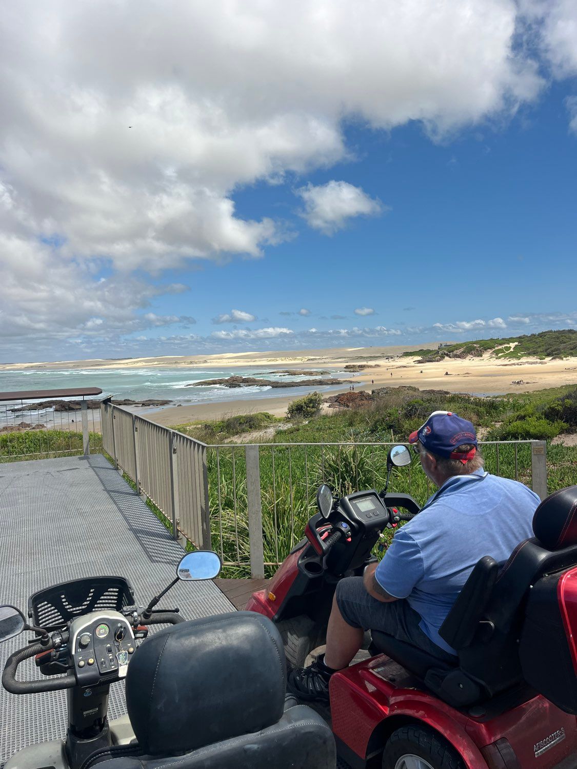 Person on a red mobility scooter overlooking a beach on a sunny day.
