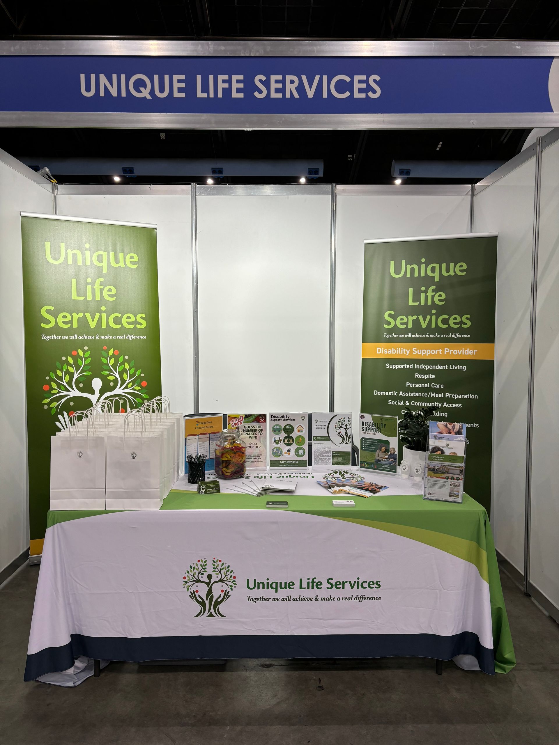 Trade show booth for Unique Life Services, green and white signage. Table with brochures.