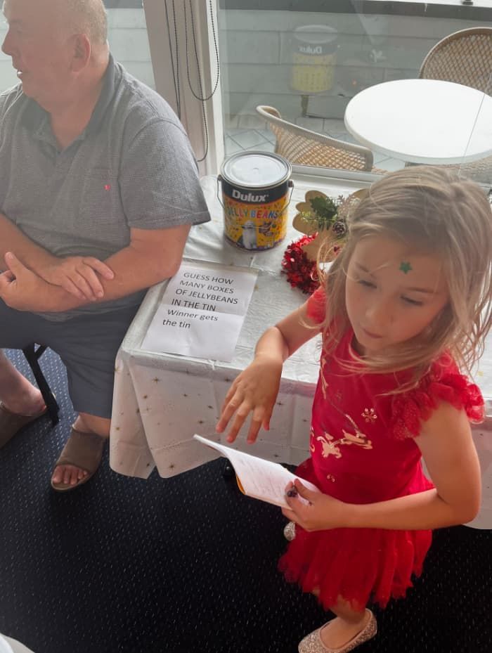 A Little Girl In A Red Dress Is Sitting At A Table With A Man — Unique Life Services In Nelson Bay, NSW