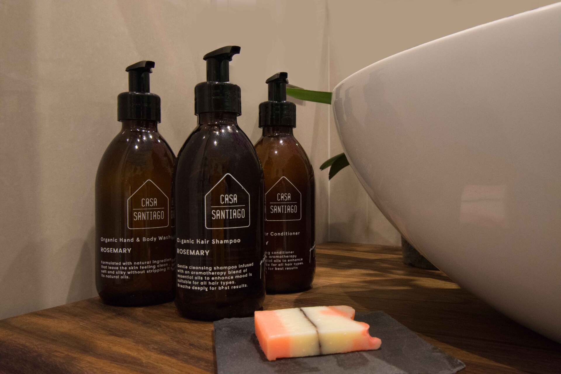 Hay tres botellas de jabón sobre una mesa de madera al lado de un lavabo.