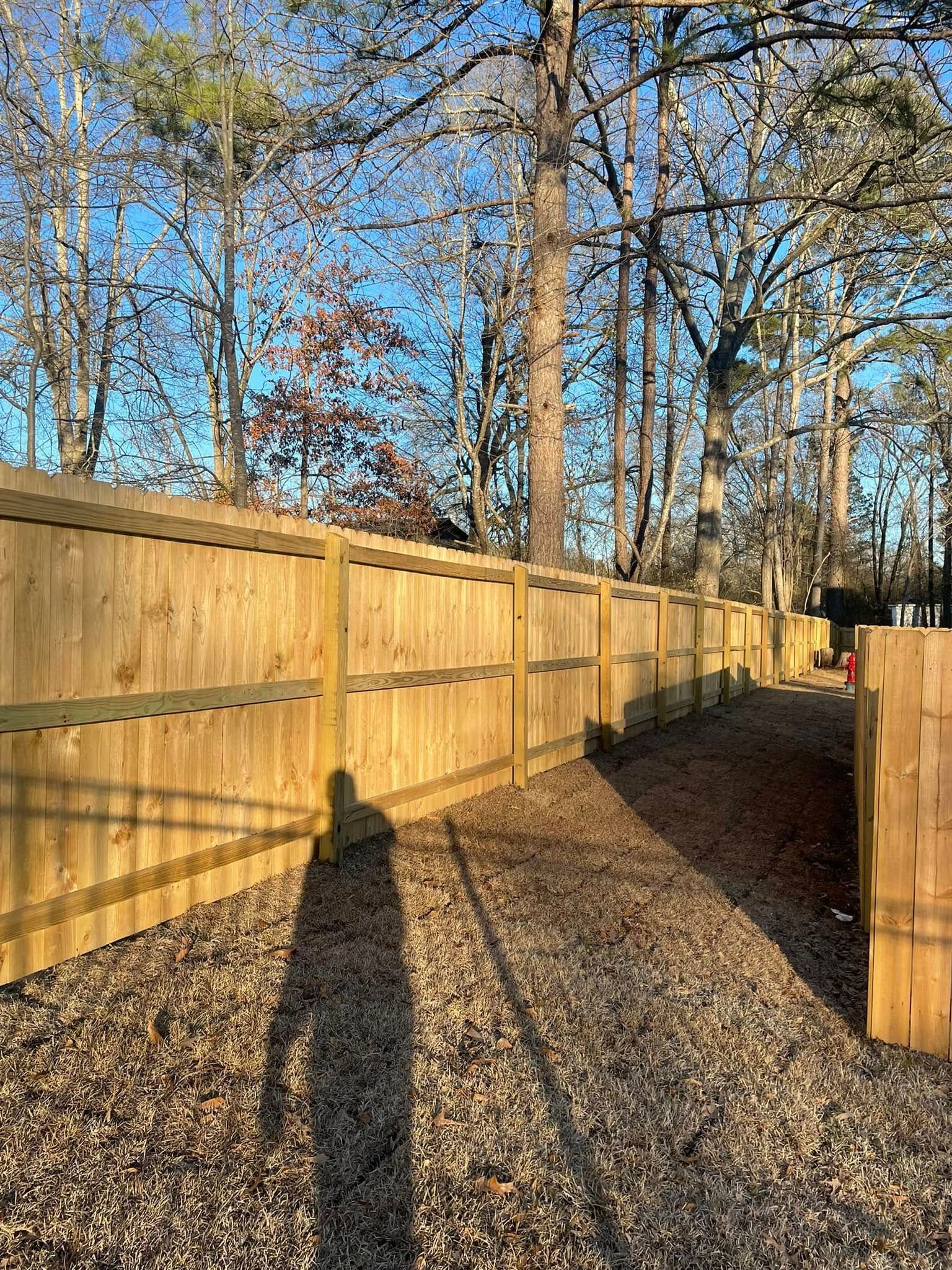 Wooden fence along a gravel path in a sunny forest setting.