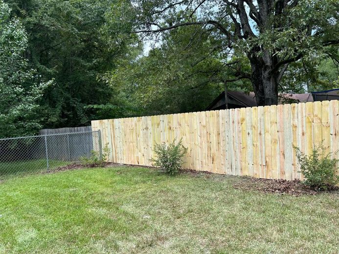 Wooden fence in a grassy backyard with a chain link fence to the left. Trees in the background.