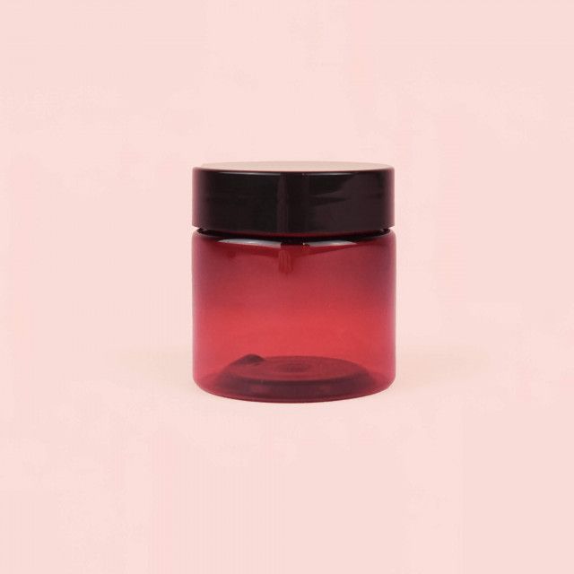 A red plastic jar with a black lid on a pink background.