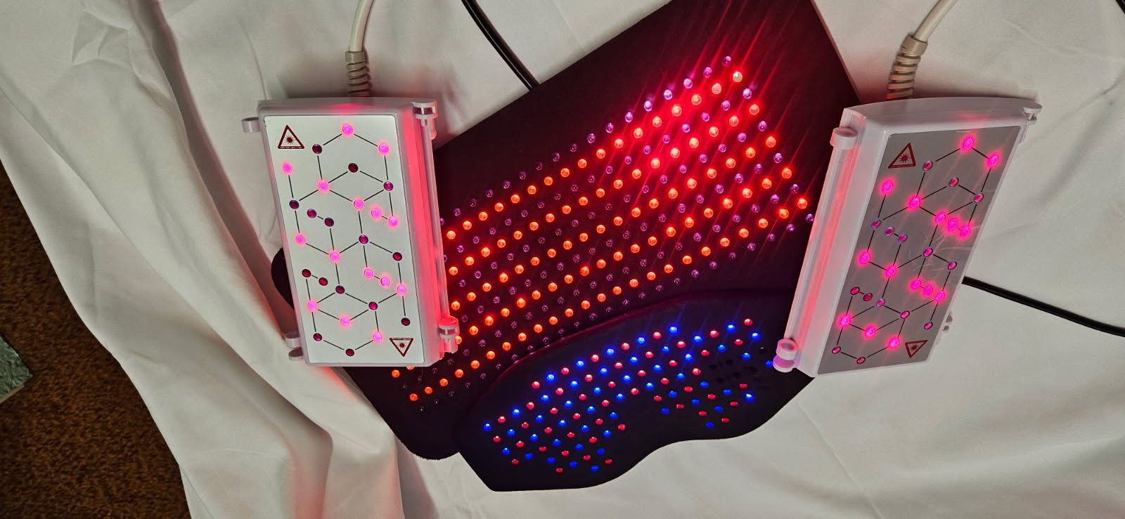 A medical device with red, orange and blue lights, and two attached control panels, lying on white fabric.