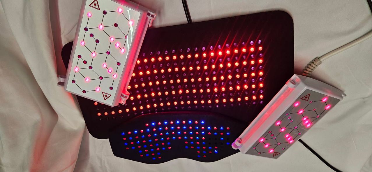A red light therapy device with a black pad and two white controllers, illuminating on a white surface.