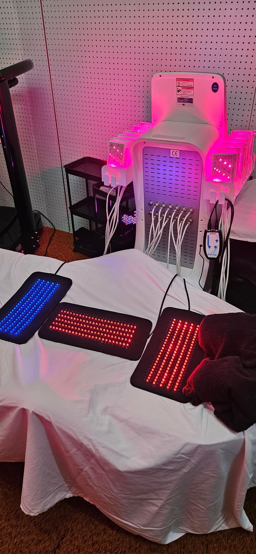 Three light therapy panels on a white draped massage table with a light therapy bed in the background.