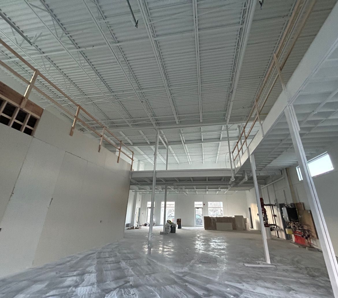 Intérieur d'un grand espace commercial inachevé, avec murs, plafond et sol en béton blancs.
