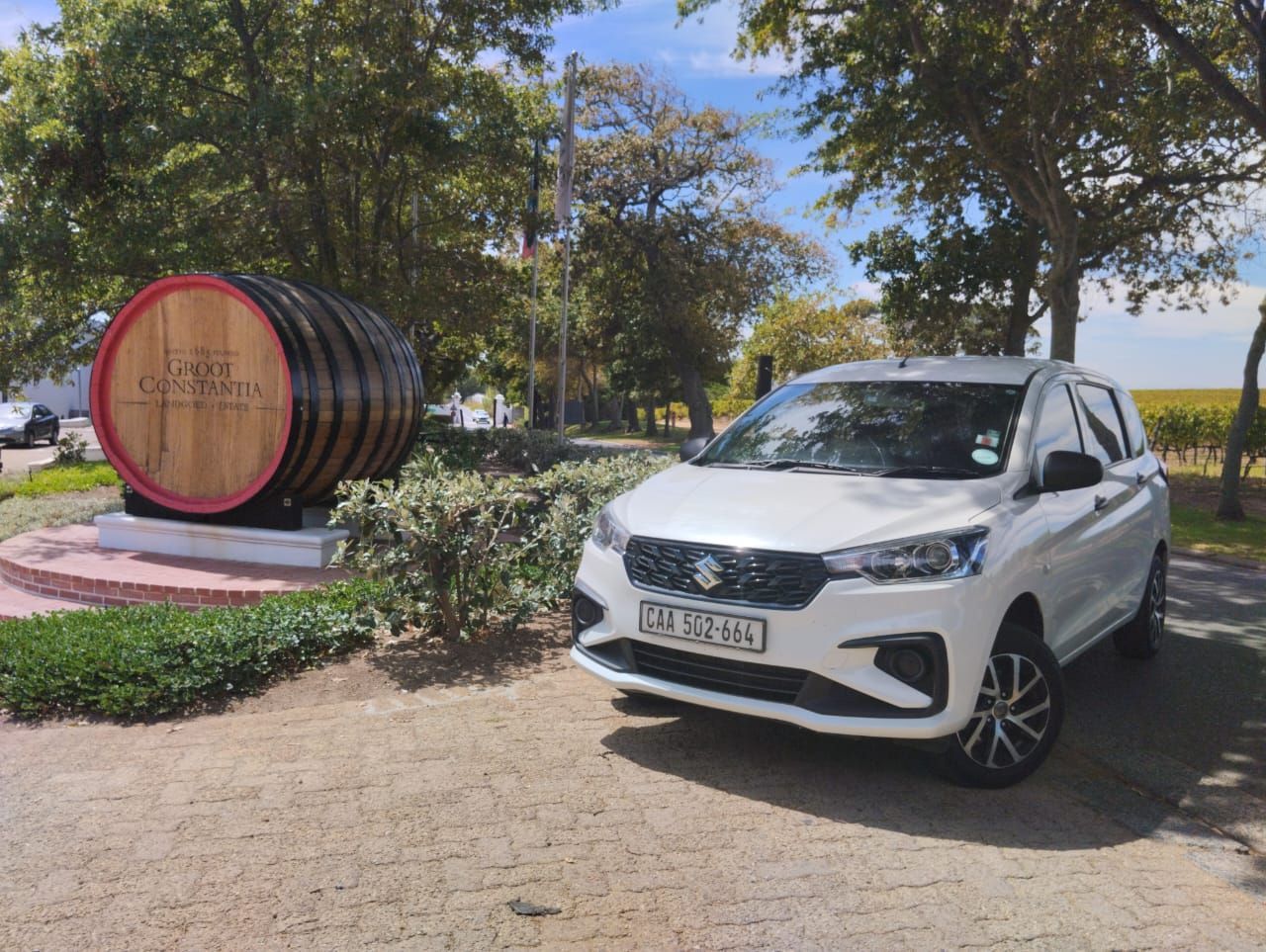A white car is parked in front of a large wooden barrel.