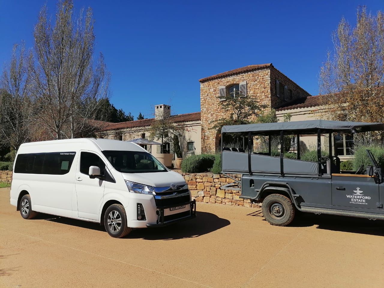 A van and a jeep are parked in front of a stone building.