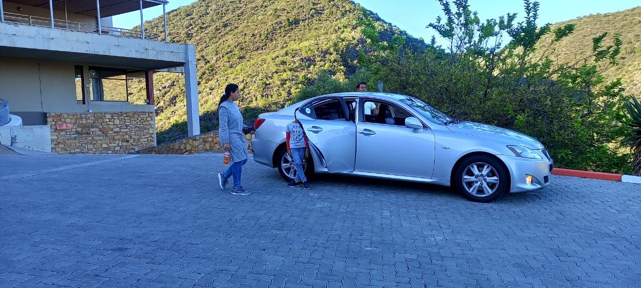 A woman is walking towards a silver car with skis in the back.