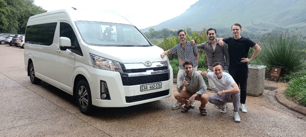 A group of men are posing for a picture in front of a white van.