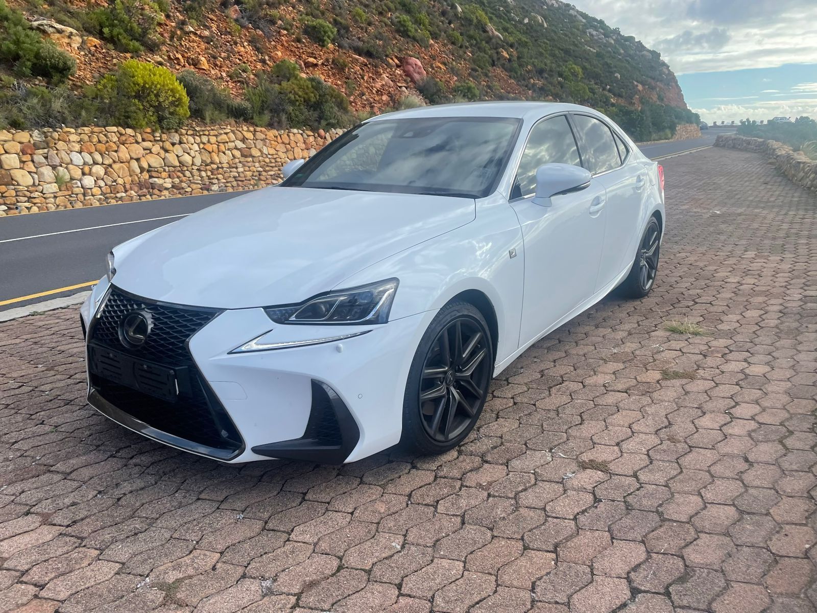 A white car is parked on a brick road next to a mountain.