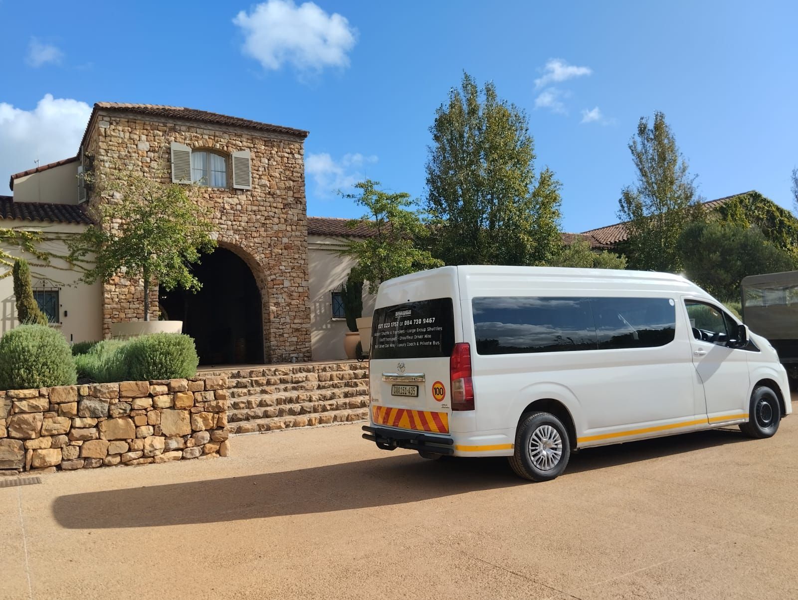A white van is parked in front of a stone building.