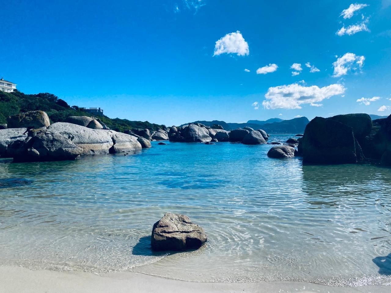 A rock is sitting on the shore of a beach next to a body of water.