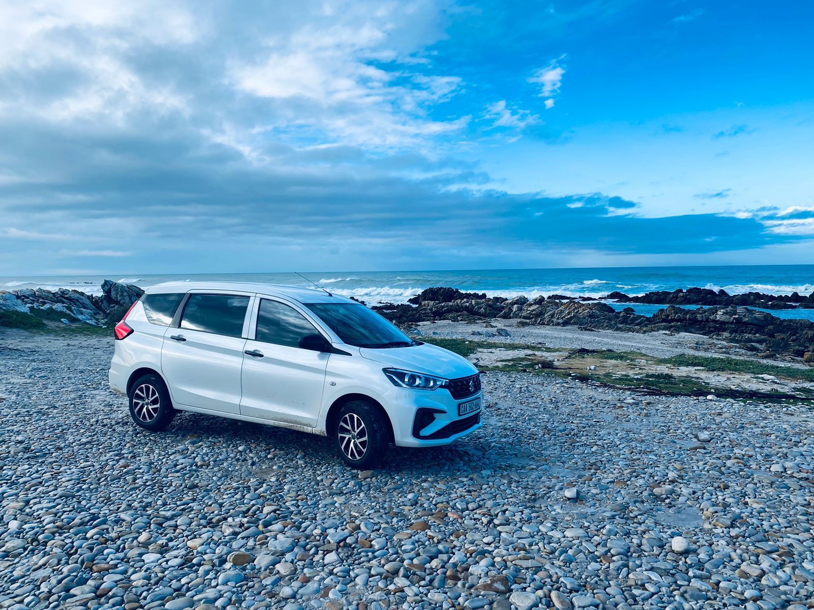 A white car is parked on a rocky beach near the ocean.