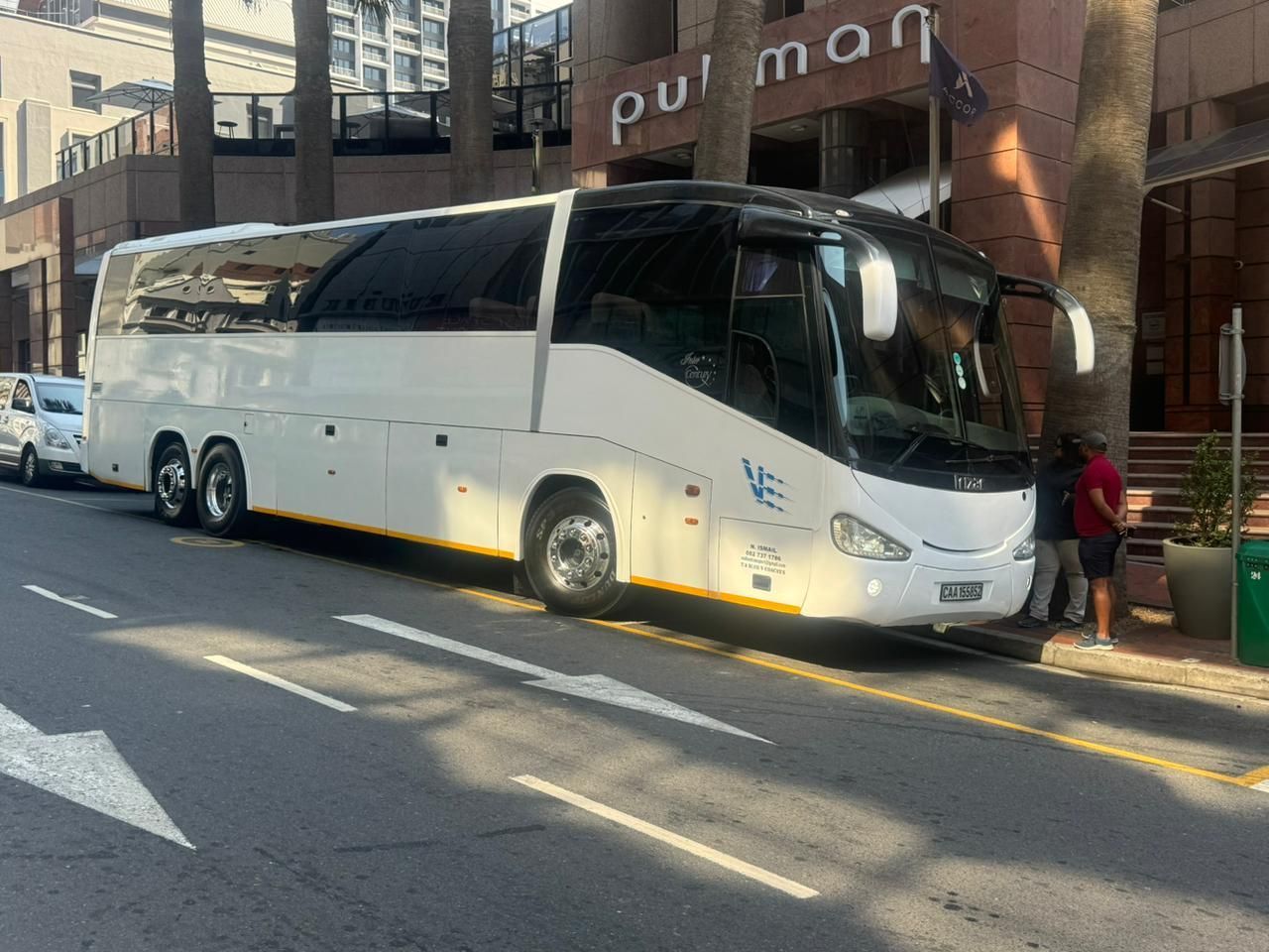 A white bus is parked on the side of the road in front of a building.