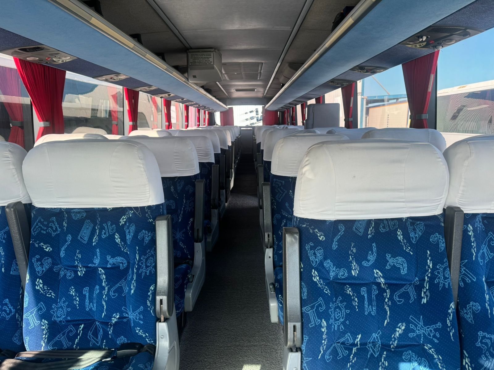 The inside of a bus with blue and white seats and red curtains.
