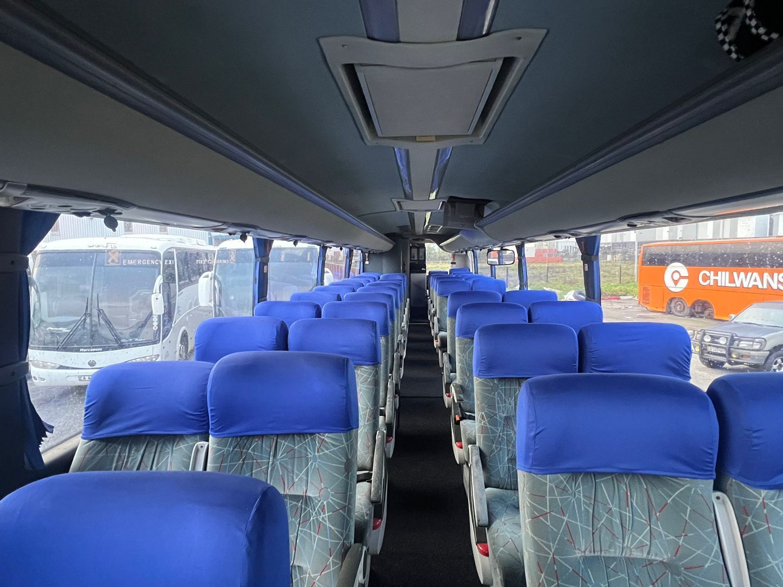 The inside of a bus with blue seats and a red bus in the background.