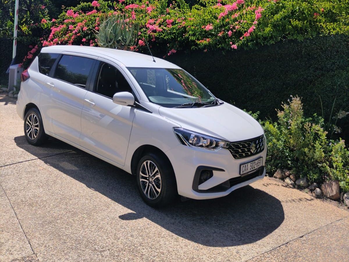 A white car is parked on the side of the road in front of a bush.