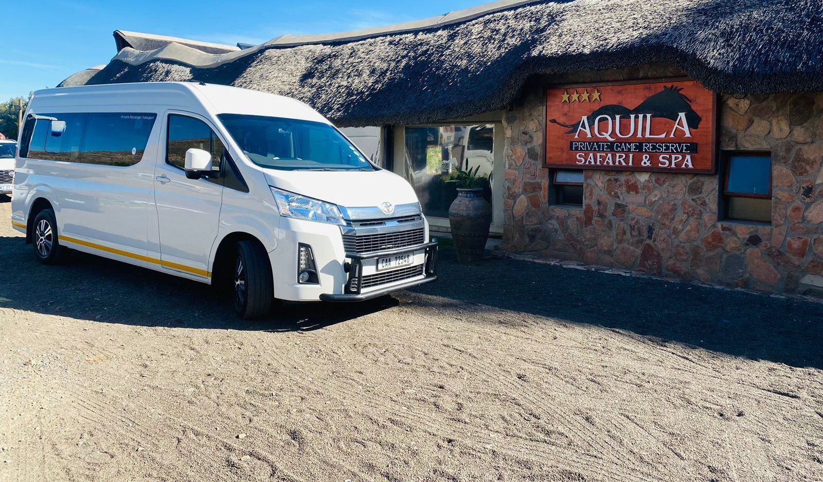 A white van is parked in front of a thatched building.