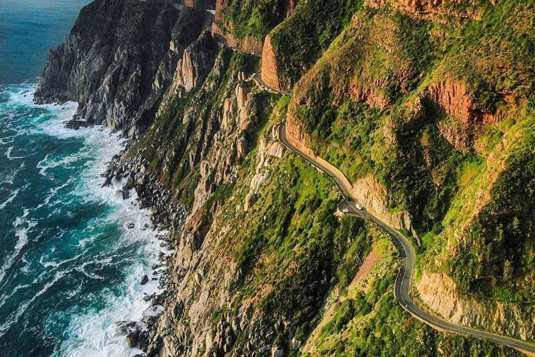 An aerial view of a road going down a cliff next to the ocean.