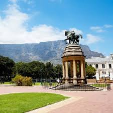 A statue of a man riding a horse in a park with mountains in the background.
