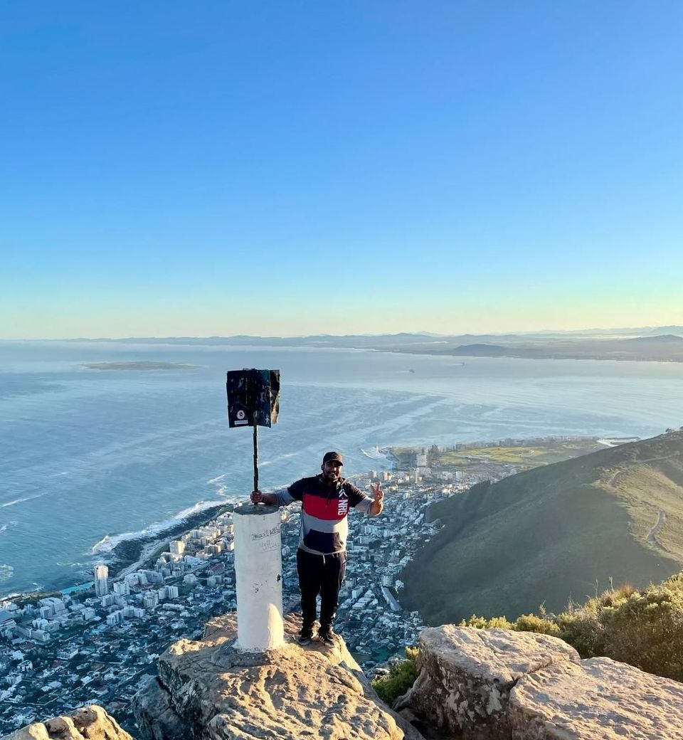 A man is standing on top of a mountain overlooking the ocean.