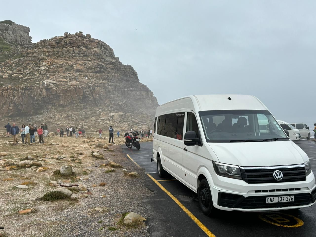 A white van is parked on the side of the road in front of a mountain.