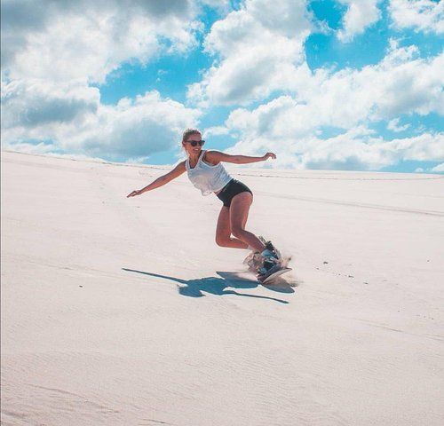 A woman is snowboarding down a sand dune.