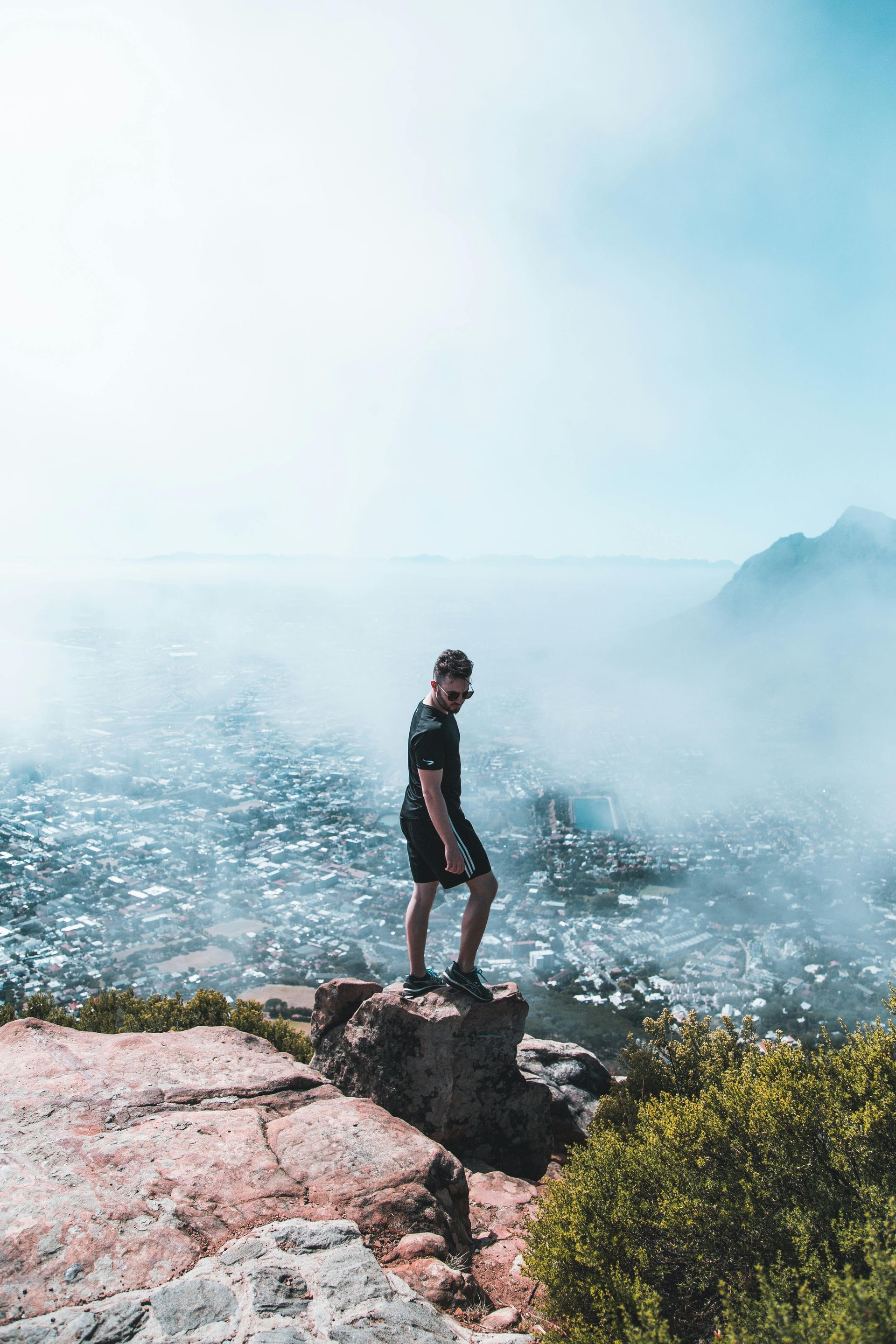 A man is standing on top of a rocky cliff overlooking the ocean.