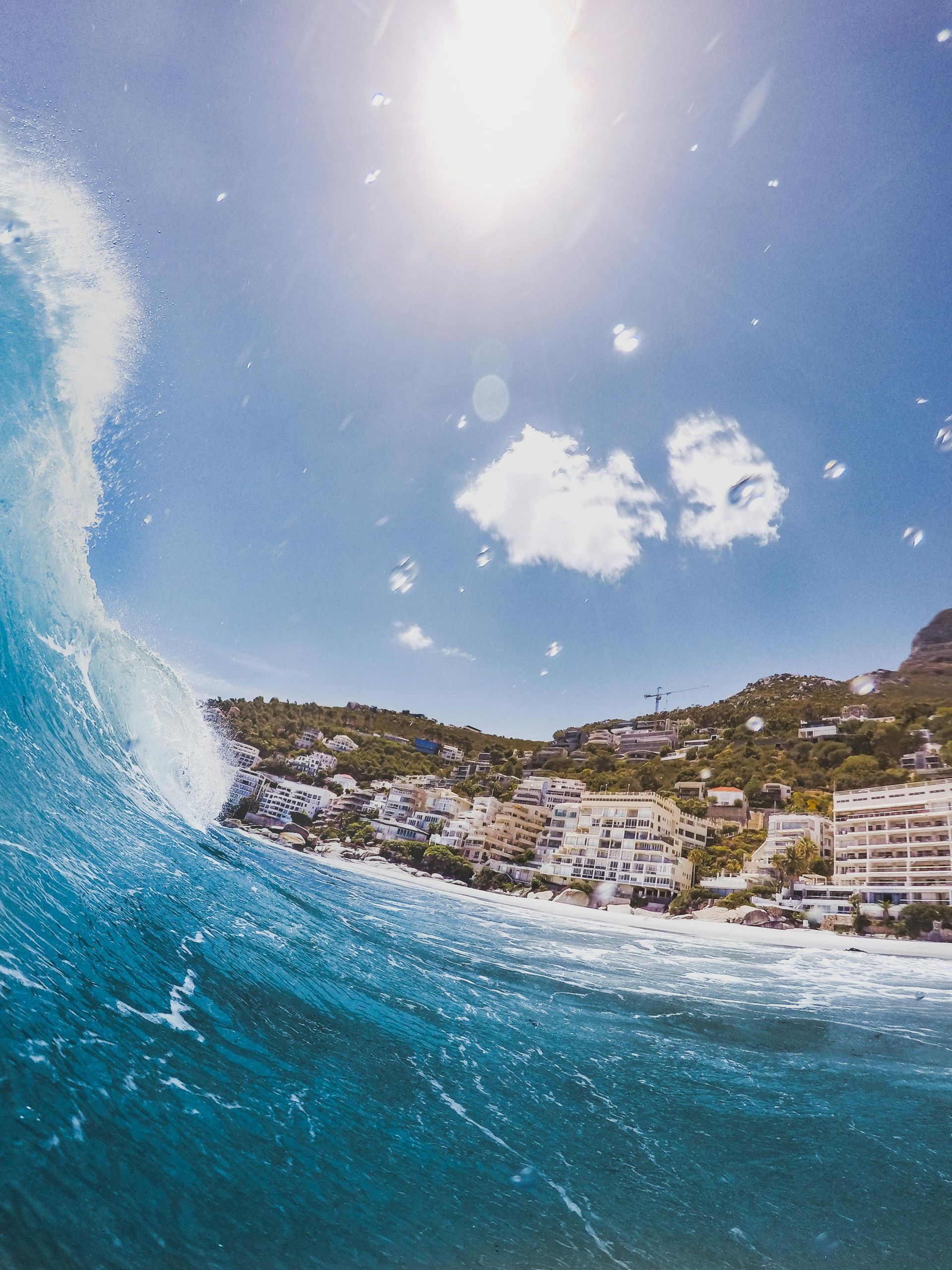 A wave is breaking on a beach with a city in the background
