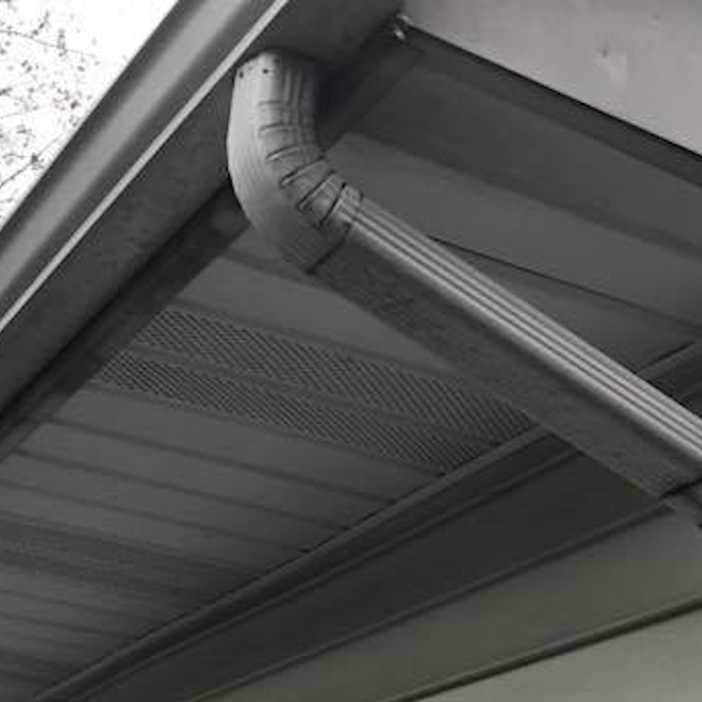 Curved gutter downspout attached to a gray metal roof under a eave.